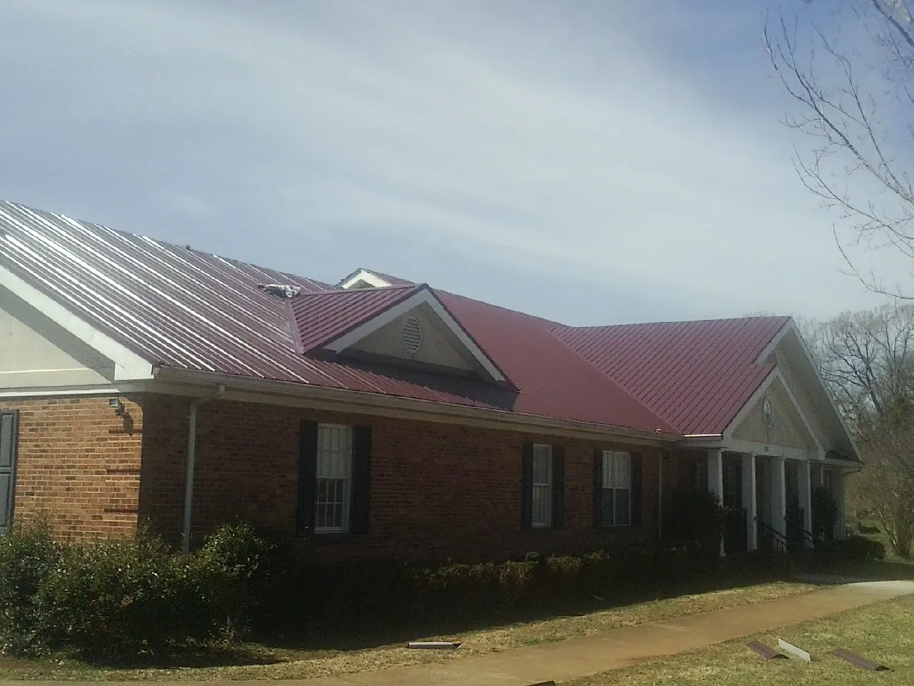 Red metal roof with gabled entries on a long brick building, from a Hail Damage Roof Repair job in Clancy