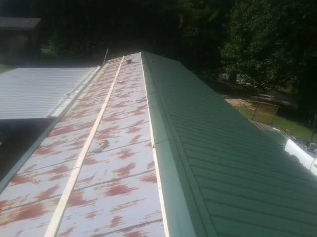 Old rusted panels beside newly installed green metal roofing — Wind Damage Roof Repair by Roofing Brothers in Clancy