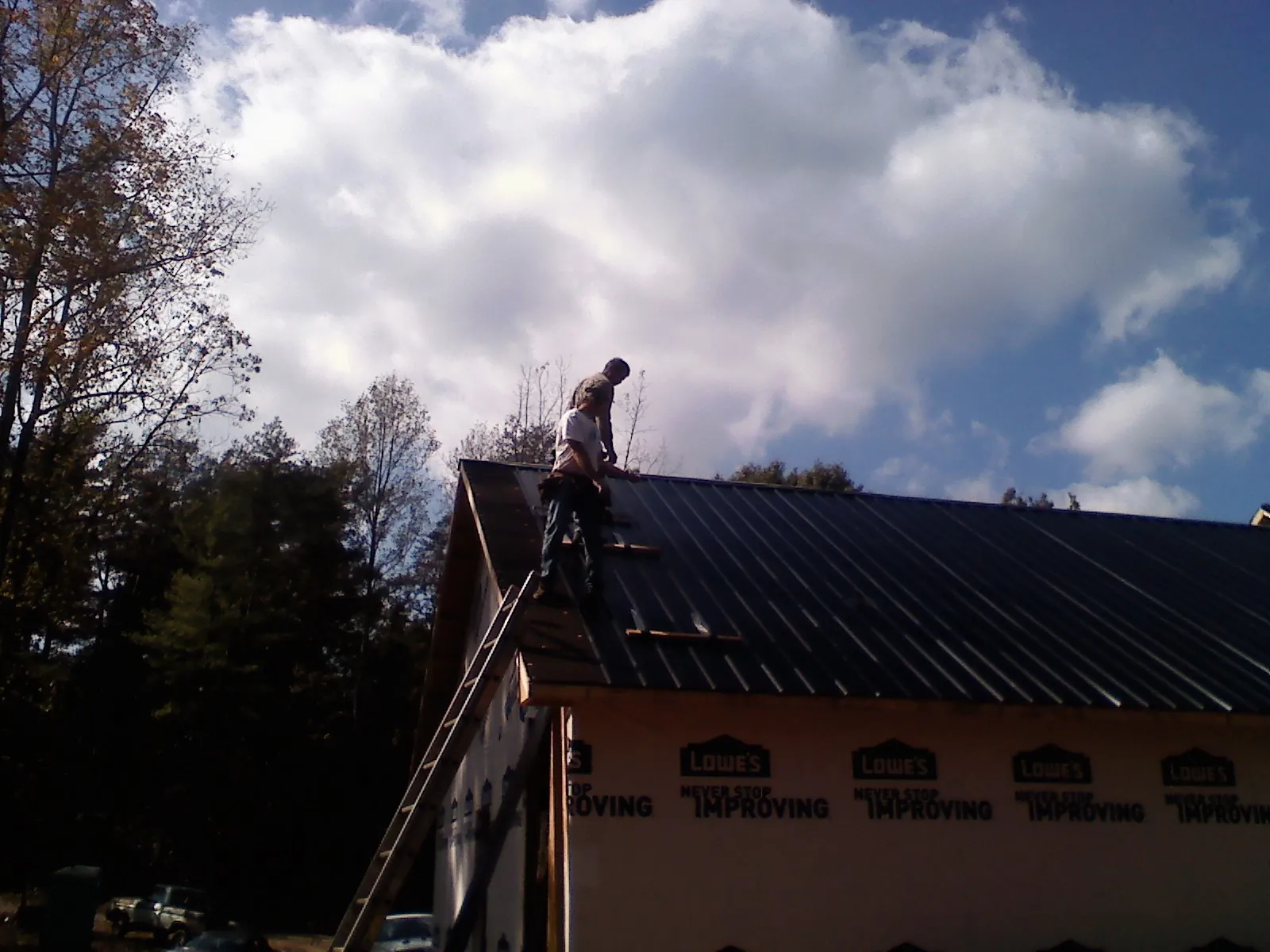 Roofer fastening dark metal panels high against a cloudy sky, from a Roof Inspection job in Clancy