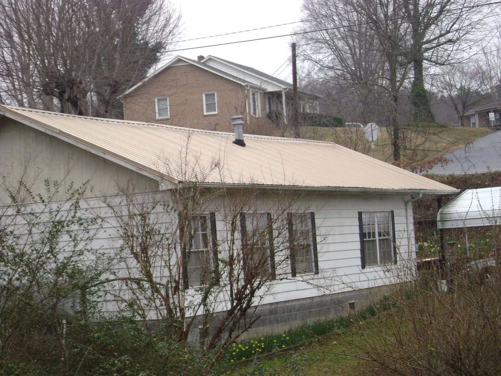 Tan metal roof on a white sided house set into a hillside — Commercial Roofing by Roofing Brothers in Clancy